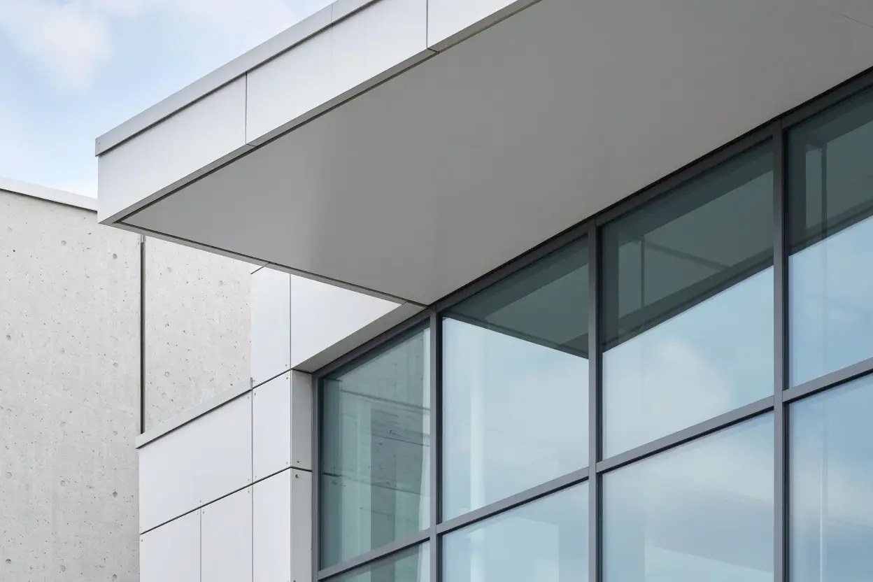 White panel and concrete facade of a modern building with a glass corner